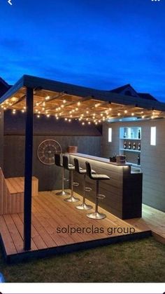 an outdoor bar with stools and lights on the roof is lit up at night