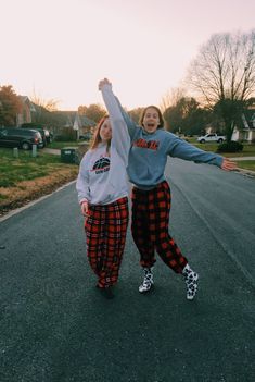 two girls are standing in the street with their arms up and one girl is wearing plaid pants