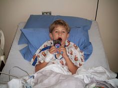 a young boy laying in a hospital bed with his mouth open and chewing on an electronic device