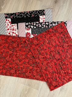 three pieces of red and black fabric sitting on top of a wooden floor next to each other