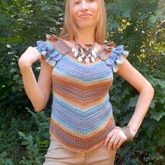 a woman standing in front of some trees wearing a crocheted top with ruffles on the shoulders