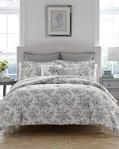 the comforter and bedding is all white with grey floral designs on it, along with two nightstands