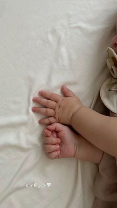 a baby laying on top of a white bed next to a pillow with its hands in the air