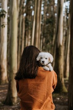 a woman in an orange jacket carrying a white dog on her back through the woods