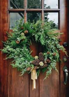 a christmas wreath on the front door with pine cones and greenery hanging from it