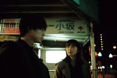 a man and woman standing in front of a train station at night with lights on