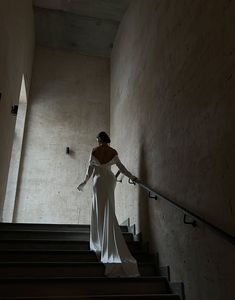 a woman in a white dress is walking down some stairs with her hand on the railing