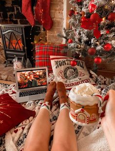 a woman is sitting in front of a christmas tree with her laptop and cup of coffee