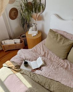 an open book on a bed in a room with wooden flooring and potted plants