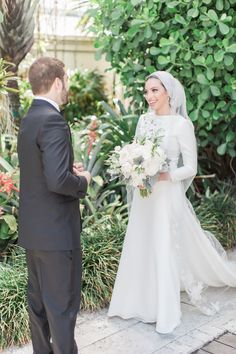 a bride and groom are standing in front of some plants, looking at each other