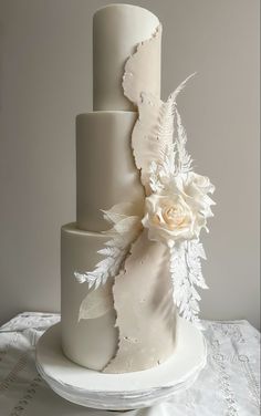 a three tiered cake with white flowers and leaves on the top is sitting on a table