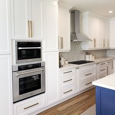 a kitchen with white cabinets and stainless steel ovens, an island in the middle