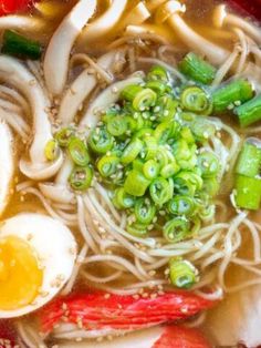 a bowl filled with noodles and vegetables next to an egg on top of some broth