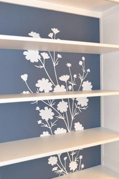 an empty shelf with flowers painted on the wall and shelves below it are white shelving units