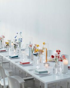 a long table is set with white chairs and flowers in vases on the tables