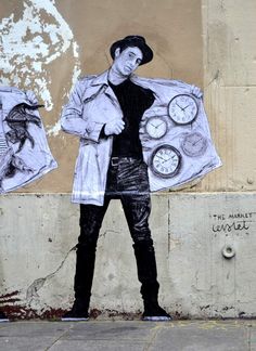 a man is standing in front of a wall with clocks painted on it and holding a jacket