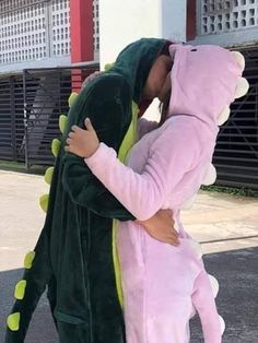 a man in a pink dinosaur costume hugging a woman wearing a green and yellow onesie