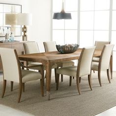 a dining room table with chairs and a bowl on it's centerpiece in front of a large window