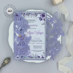 a purple wedding card on a plate next to some ribbon and a bottle of wine