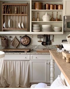 a kitchen filled with lots of white cupboards and dishes on top of wooden shelves