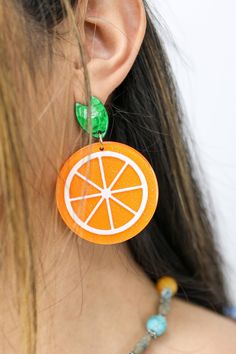 Our Fresh Citrus Earrings feature an orange citrus design that is sure to brighten up any look. The lightweight construction and high quality resin make these earrings comfortable and resilient. Step out in style with these beautiful and unique earrings. Details:- Sparkling Orange Slice Drop Earrings- Stud Post BackingDimensions:- Length Approx. 2.5"- Width Approx. 1.75" Orange Earrings For Summer Gifting, Summer Orange Drop Earrings, Summer Orange Jewelry With Fruit Design, Trendy Orange Drop Earrings, Trendy Orange Plastic Jewelry, Trendy Orange Dangle Earrings, Trendy Orange Round Earrings, Orange Dangle Resin Earrings, Orange Resin Dangle Earrings