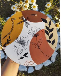 a hand holding a paper plate with flowers and dragonflys on it in front of daisies