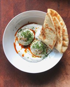 an egg and pita on a white plate with some sauce in the bowl next to it