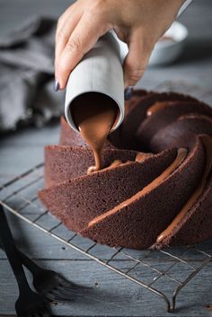 someone pouring chocolate frosting on top of a bundt cake