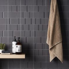 a towel and some bottles on a shelf next to a wall that has grey tiles