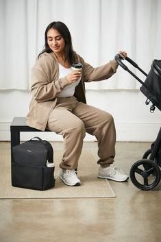 a woman sitting on top of a luggage bag next to a baby stroller and holding a cup