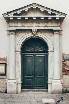 two pigeons sitting on the ground in front of a building with an arch and doorway