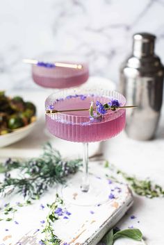 two cocktails sitting on top of a table next to plates with flowers and herbs