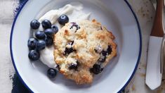 a blueberry muffin on a white plate with whipped cream and fresh blueberries