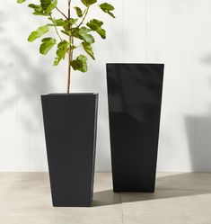 two tall black vases sitting next to each other on top of a cement floor