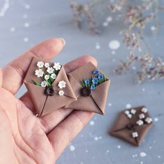 someone is holding two small origami flowers in their hands, one has blue and white flowers on it