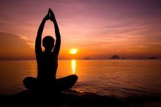 a person doing yoga in front of the ocean at sunset with their arms raised up