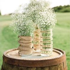 two vases filled with baby's breath flowers on top of a wooden barrel