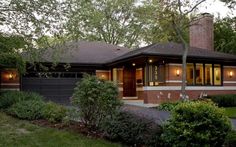 a brick house with lots of windows in the front yard and trees on both sides