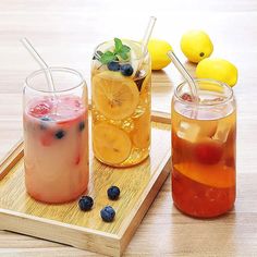 three drinks are sitting on a tray with lemons and blueberries