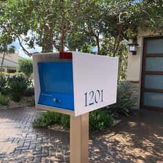 a blue and white mailbox sitting on top of a brick sidewalk next to a tree