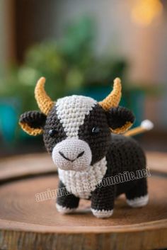 a small crocheted cow is standing on a wooden table with it's head turned to the side