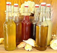 four bottles of different types of liquid on a table with shells and flowers in the background