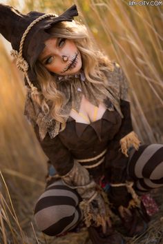 a woman dressed up as a witch sitting in the middle of tall grass with her hands on her hips