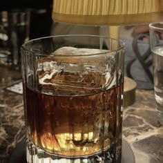 a glass filled with liquid sitting on top of a table next to a lamp shade