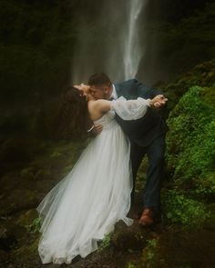 a bride and groom kissing in front of a waterfall