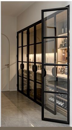 an open glass door in the middle of a room with wine bottles on shelves behind it