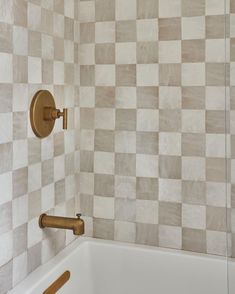 a bath tub sitting next to a tiled wall with wooden handles on the faucet