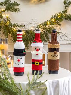 three wine bottles decorated like santa claus, snowman and elf hats on a table