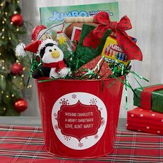 a red bucket filled with lots of holiday treats on top of a table next to a christmas tree