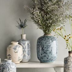 three vases with flowers in them sitting on a shelf next to other vases